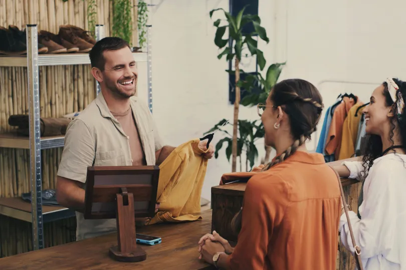 Fashion, cashier and man in shop with customer, small business sales with friendly smile at pos and shopping