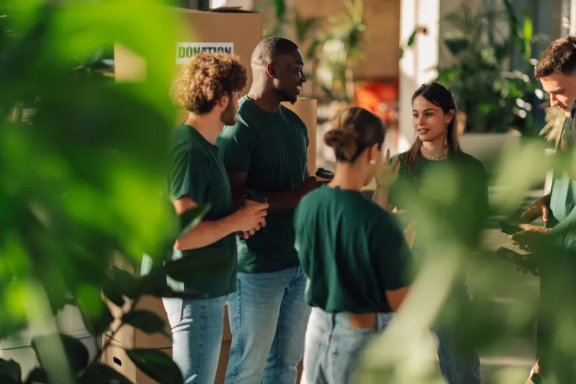 Group of diverse volunteers wearing green t-shirts discussing during donation drive in modern office