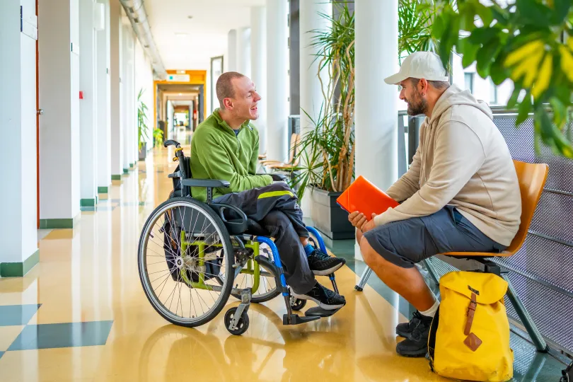 Man with physical disability in wheelchair and friend chatting in a modern building