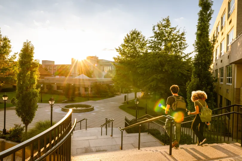 Two university students walk down campus stairs at sunset