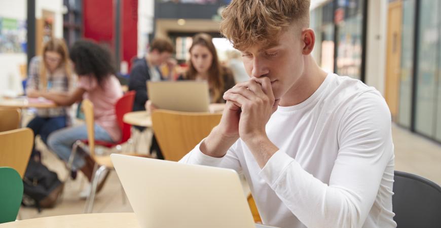 Jeune homme dans la bibliothèque avec son ordinateur portable