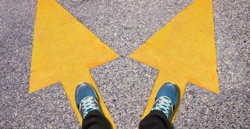 Person standing on two arrows pointing in different directions