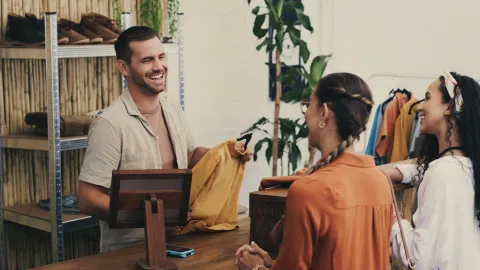 Fashion, cashier and man in shop with customer, small business sales with friendly smile at pos and shopping