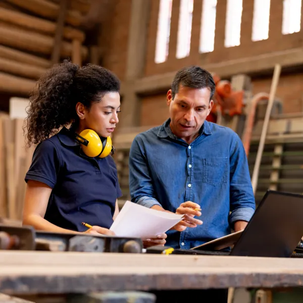 Foreman talking with a female apprentice at a wood factory while looking at a design