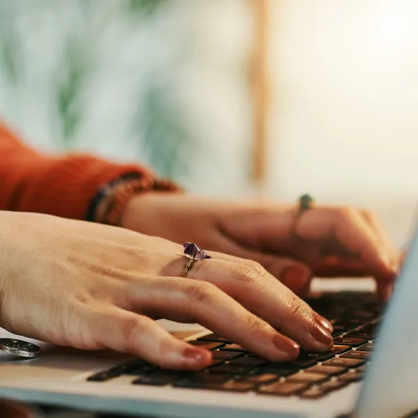 A close-up shot of hands typing on a laptop keyboard, bathed in warm sunlight