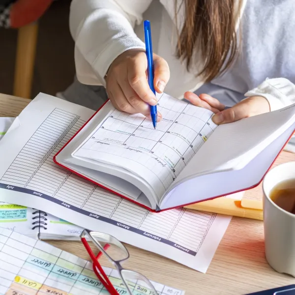 Close-up Of A woman writing schedule In calendar notebook on a desk with paperwork and coffee cup