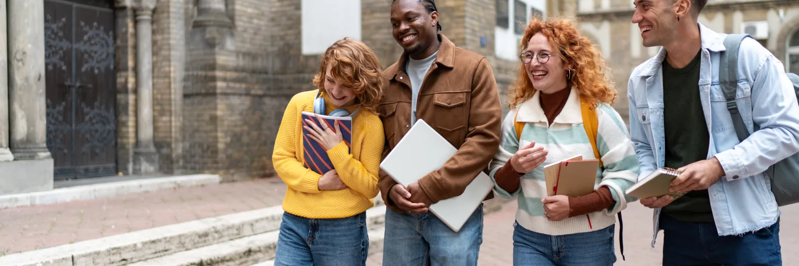 A group of diverse university students walking in college campus carrying books and talking